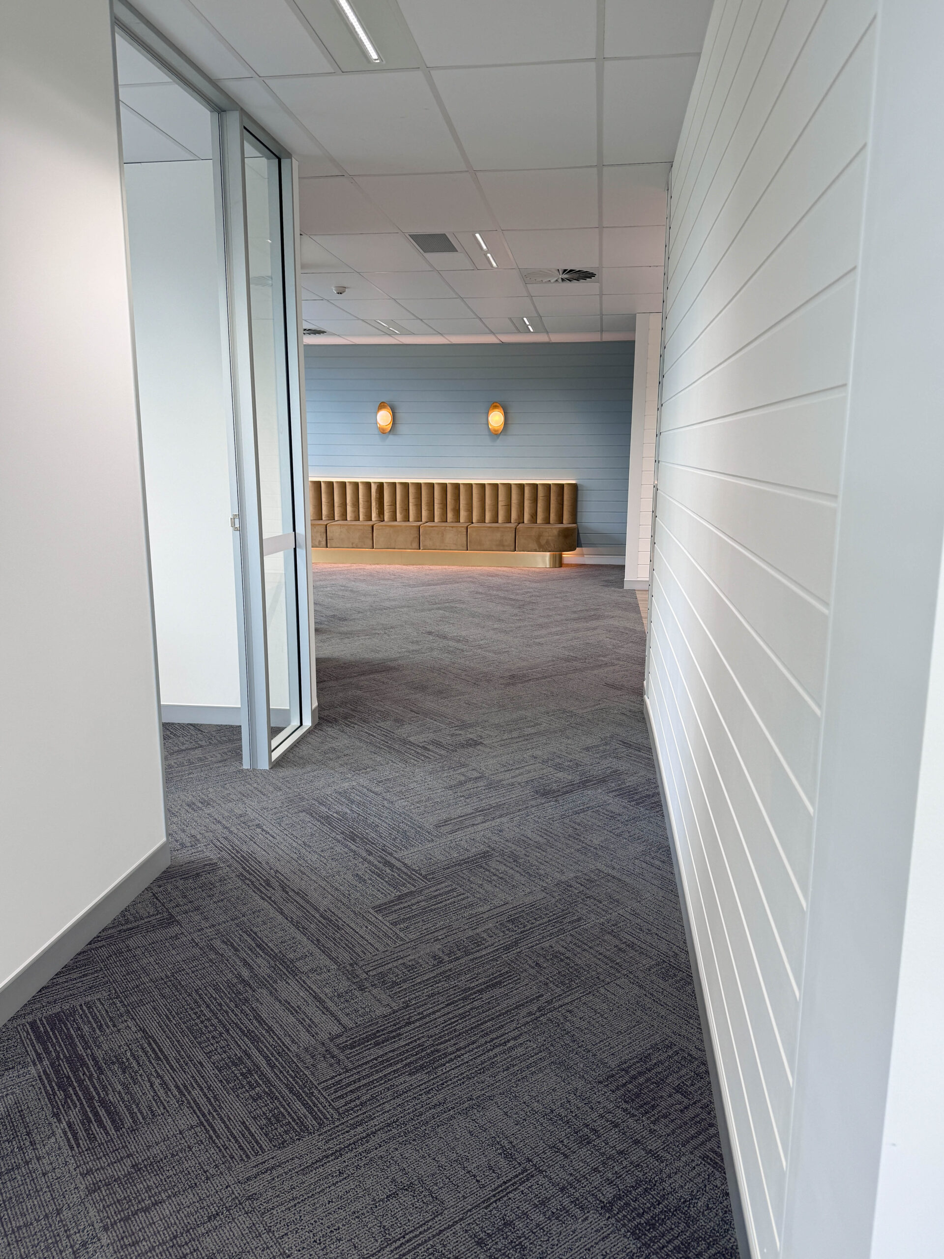 Clinic corridor leading to the waiting area with carpet flooring, glass partition and wall panelling