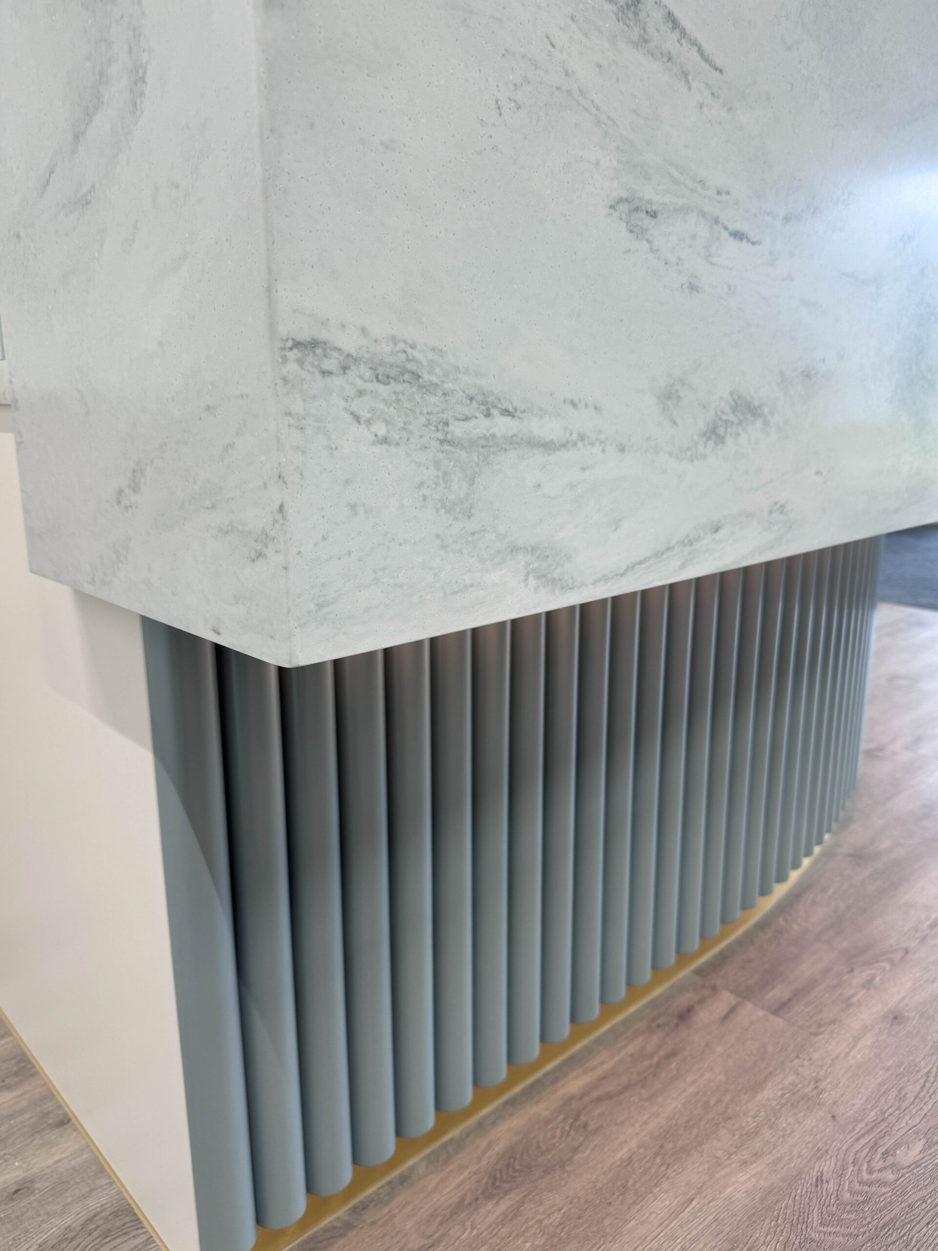 Close-up of reception desk joinery with stone-look counter and vertical fluted panelling.