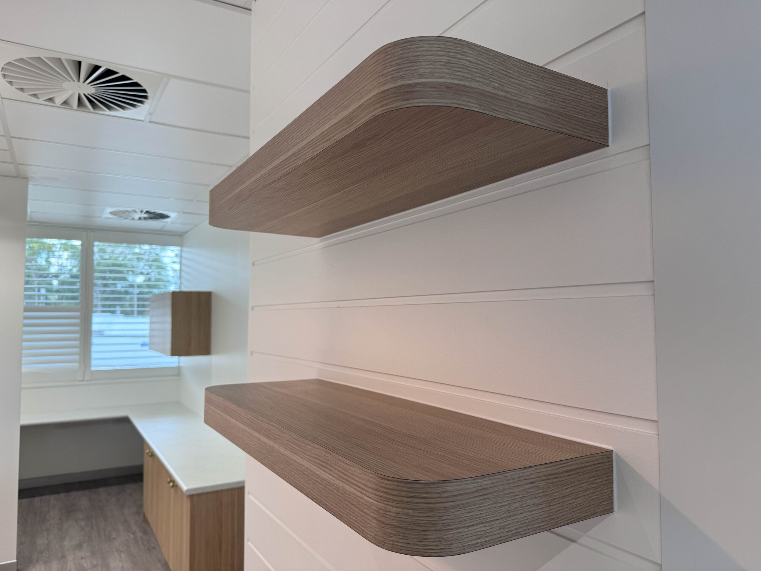 Floating timber shelves and white wall panelling detail within a healthcare clinic interior