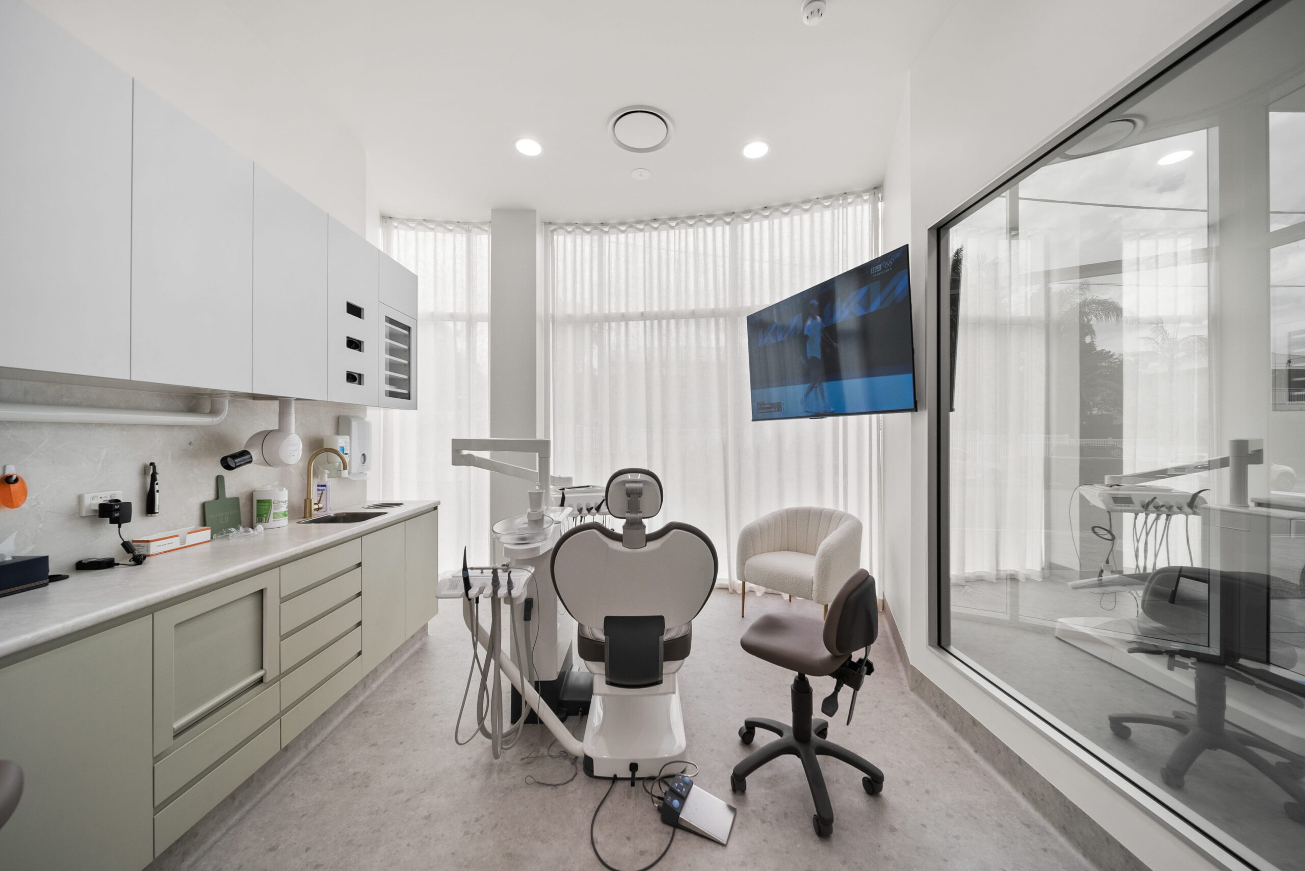 Treatment room with a patient chair, integrated cabinetry and large windows allowing natural light.