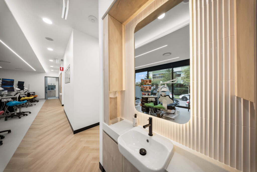 Backlit mirror and feature wall with integrated lighting beside a naturally lit dental treatment area