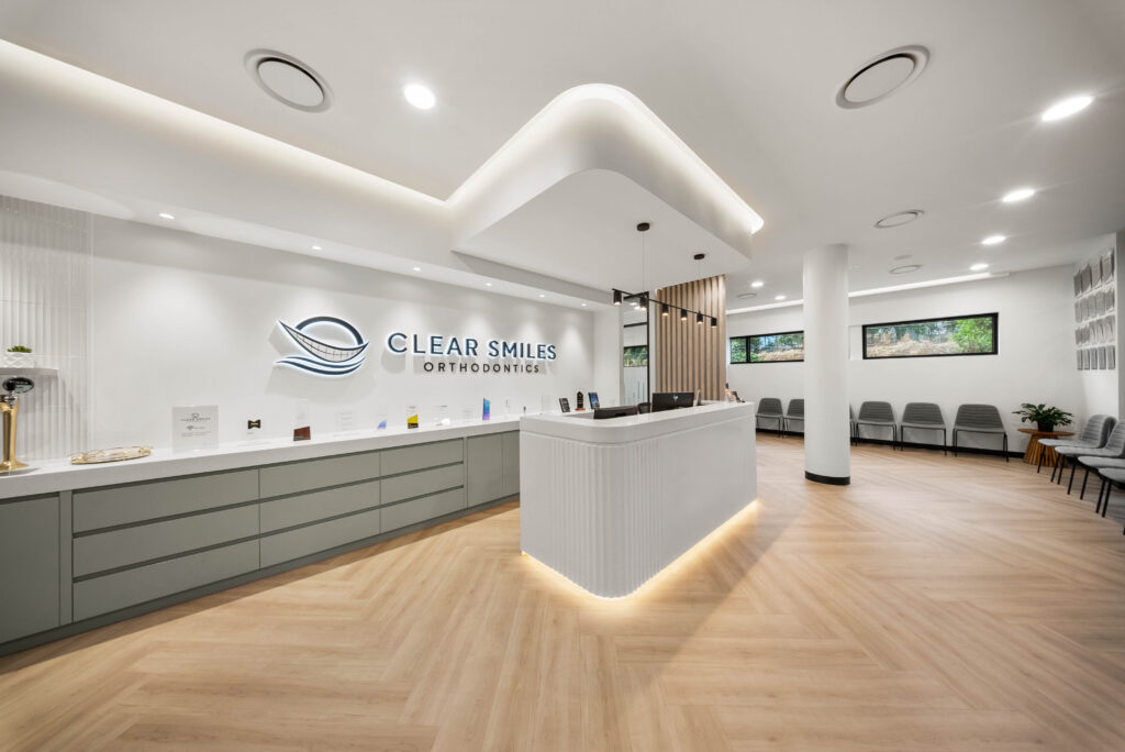 Modern dental clinic reception with layered ceiling lighting, illuminated reception desk and branded feature wall.