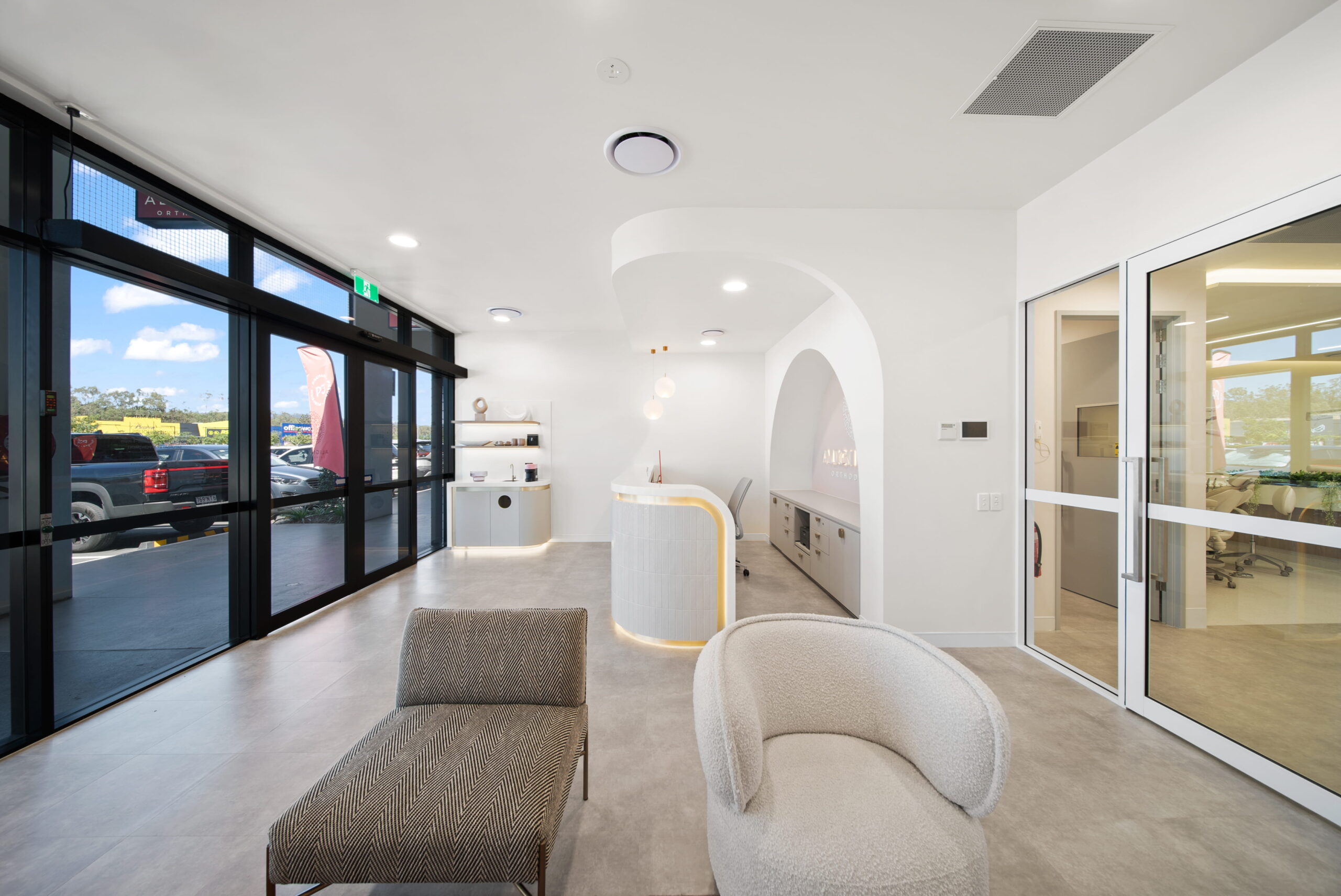Bright orthodontic reception and waiting area with curved desk, accessible entrance and treatment rooms beyond